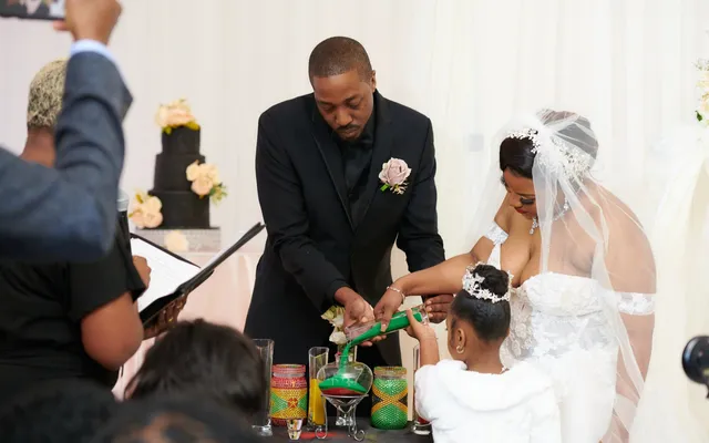 A groom, a bride and a young girl pour sand together from jars decorated in green and gold beads
