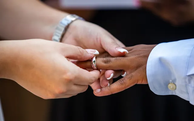 Close-up of one partner sliding a wedding band onto the other's finger