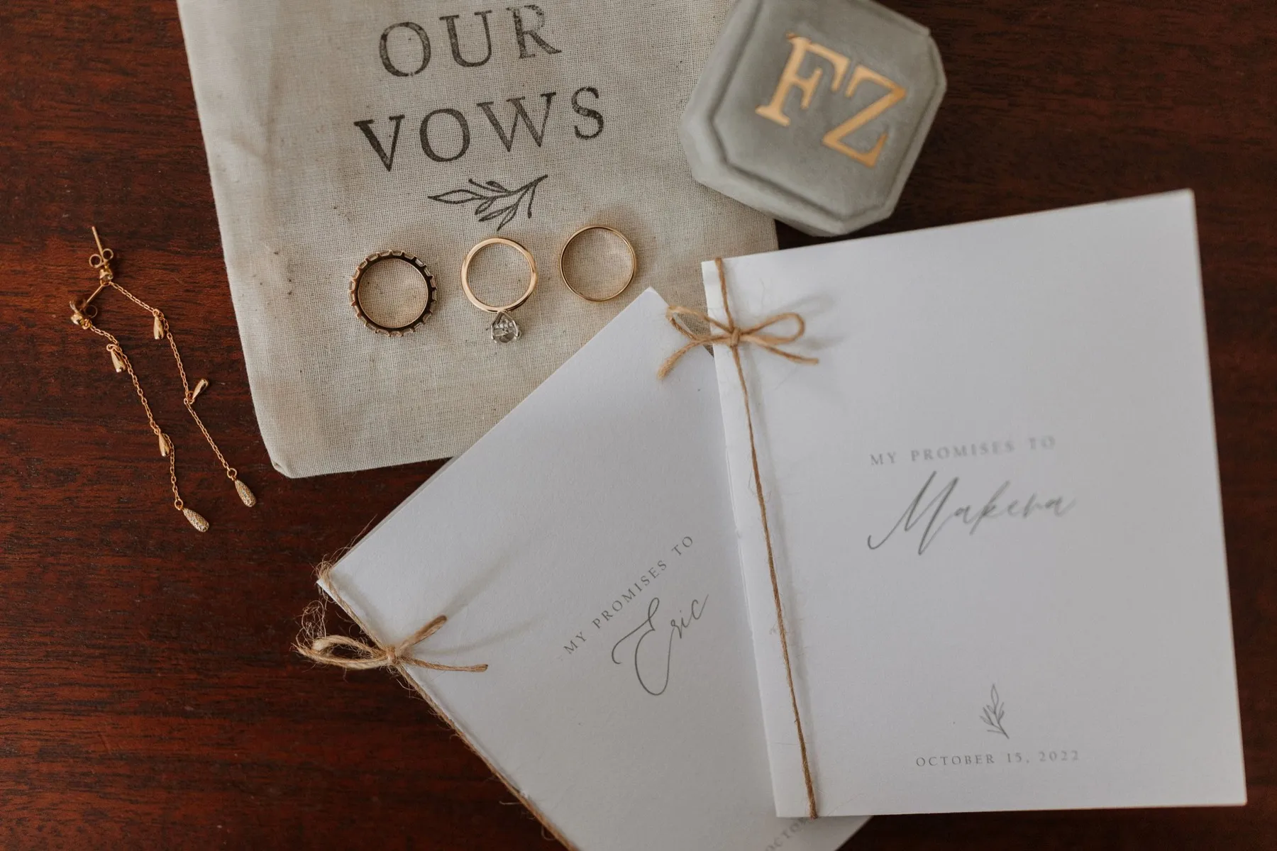 Two handmade vow booklets tied with twine beside a linen pouch printed with the words Our Vows and three rings
