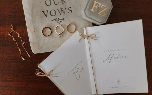 Two handmade vow booklets tied with twine beside a linen pouch printed with the words Our Vows and three rings