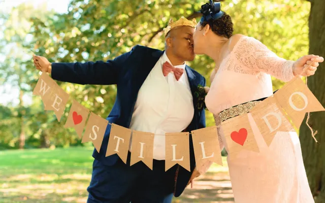 A couple kisses behind a burlap banner that reads We Still Do