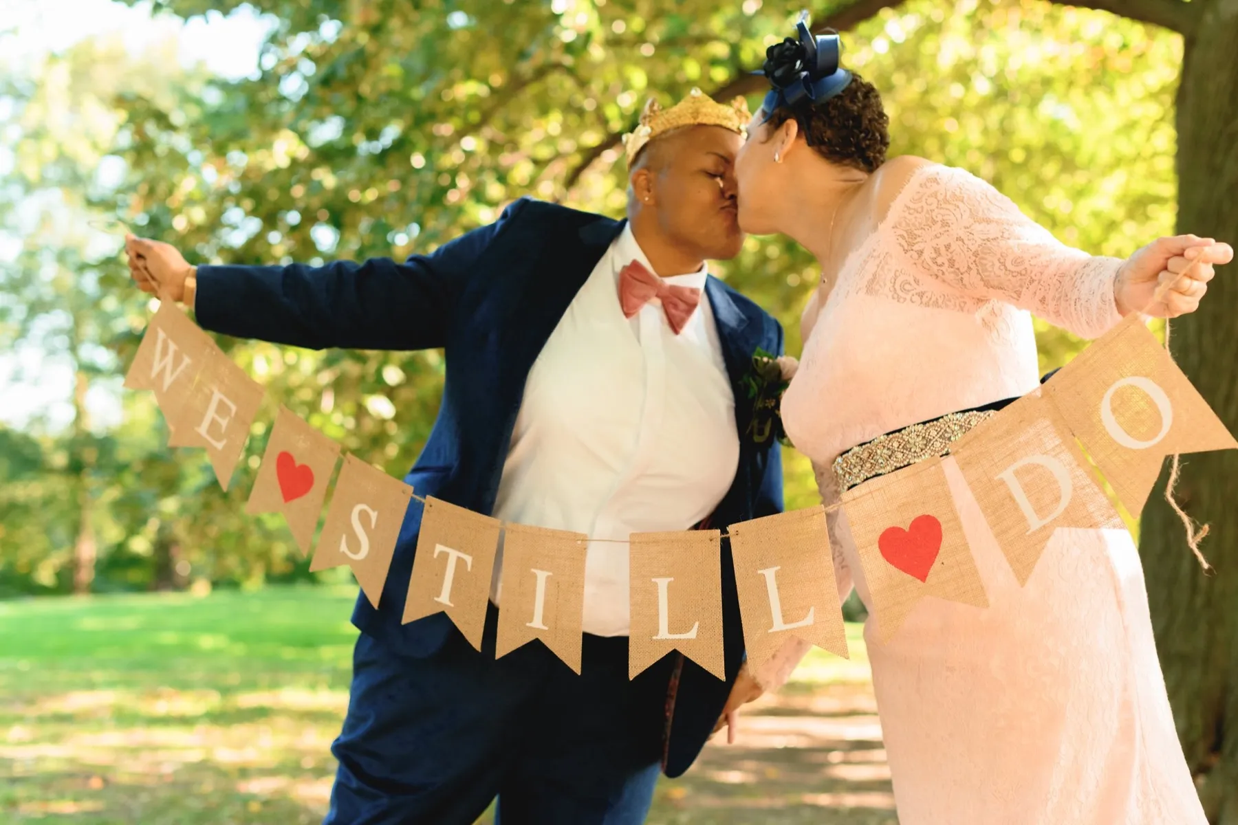 A couple kisses behind a burlap banner that reads We Still Do