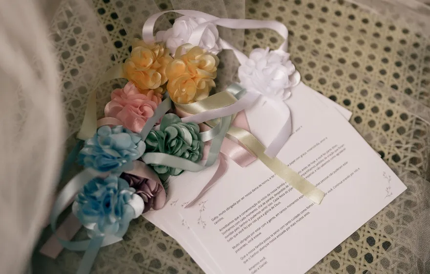 A printed program on a cane-backed chair draped in tulle, a ribbon of pastel fabric flower hair pieces laid across it