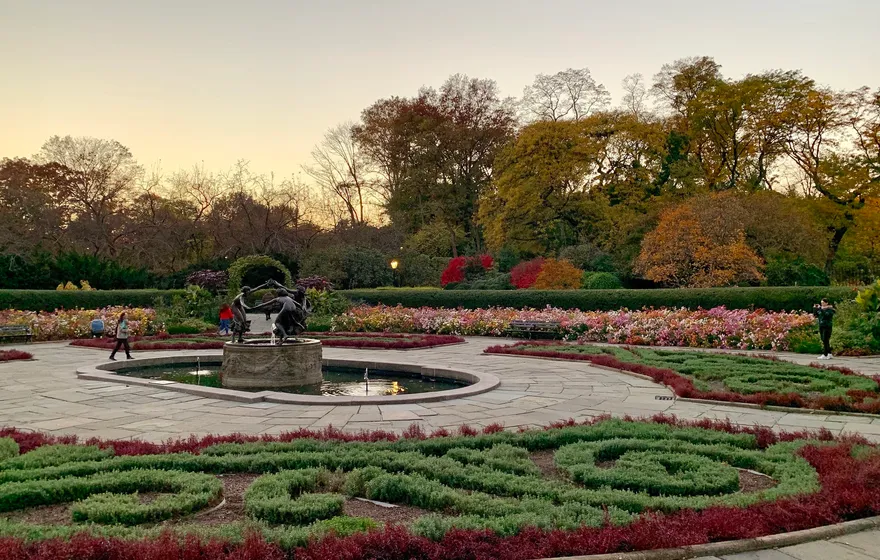The North Garden at dusk in autumn, curving parterre beds of red flowers around the Untermyer Fountain with turning trees behind