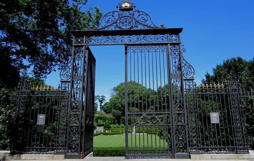 The black wrought-iron Vanderbilt Gate of the Conservatory Garden standing open, with the green lawn of the Center Garden visible through it